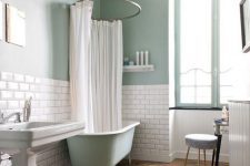 an eclectic bathroom with green walls and white subway tiles, a green clawfoot tub, a pedestal sink, a round stool and a vanity is glam