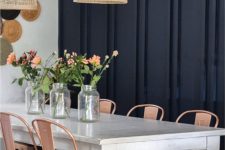 an eclectic dining space with a black paneled wall, a vintage white table, copper chairs, woven lamps and decoative plates