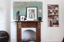 an eclectic living room with a grey sofa, a fireplace wiht a shabby chic mantel, some artworks and books inside the fireplace