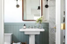 an elegant bathroom with green panelling, a pedestal sink, a wooden ladder, a mirror in a wooden frame and vintage sconces