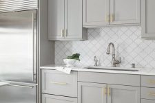 an elegant dove grey kitchen with shaker cabinets, gold handles, a white arabesque tile backsplash and gold and chrome touches