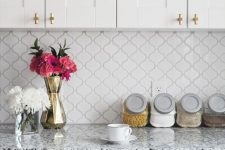 an elegant white kitchen with shaker cabinets and gold fixtures, a small scale arabesque tile backsplash and terrazzo countertops is very cool
