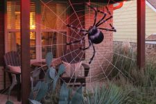 02 a back porch decorated with a giant spiderweb and a fluffy spider is a cool idea to style your outdoor space for Halloween without much effort