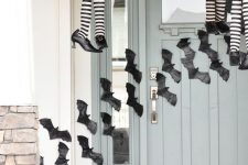 03 black paper bats attached to the wall and door, witches’ legs and black candle lanterns and orange pumpkins make the porch Halloween-like
