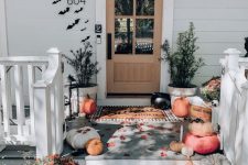 05 a beautiful Halloween front porch with natural pumpkins and skulls, potted greenery, black paper bats on the wall around the door