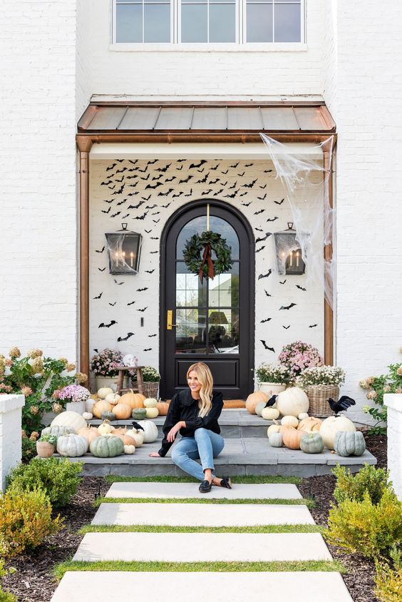 a farmhouse front porch done with lots of heirloom pumpkins, blooms in baskets and black paper bats covering the wall is amazing