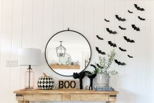 11 a modern farmhouse space with black paper bats attached to the wall, a wooden console with a black cat, BOO, a black and white printed pumpkin