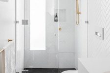 12 a small contemporary bathroom with white chevron tiles on the walls, black hex tiles, gold fixtures and a long and narrow window with frosted glass