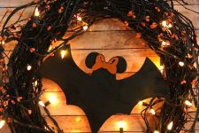 22 a black vine Halloween wreath with lights, orange blooms, a large black paper bat is a cool solution to DIY easily
