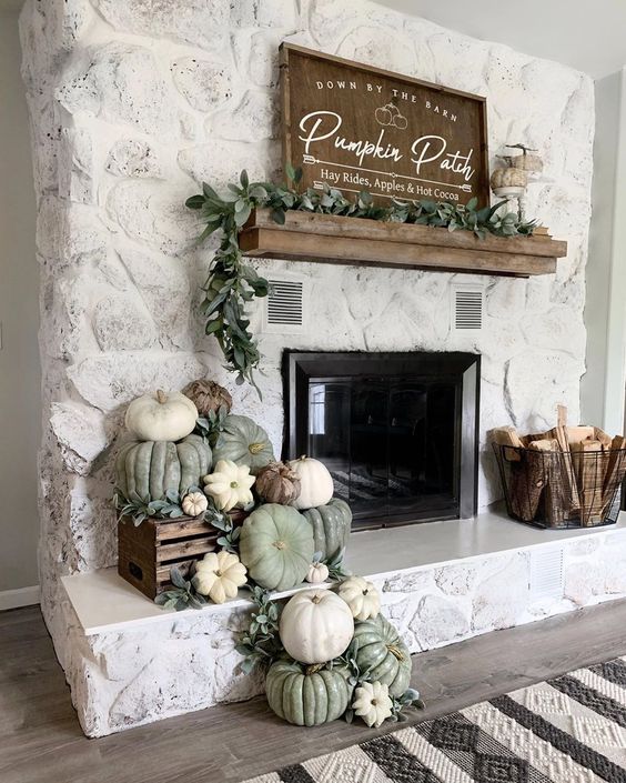 rustic fireplace styling with heirloom pumpkins and greenery in a crate, a wire basket with firewood and a greenery garland on the mantel