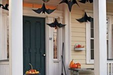 33 a Halloween porch with black paper bats hanging down, orange and neutral pumpkins on the floor, bench and steps is cool
