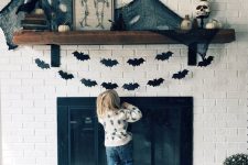 35 a Halloween mantel decorated with black paper bat buntings, black spider web and pumpkins plus skulls