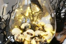 a Halloween terrarium of a large jar, skulls and lights, branches and spiderweb, a blackbird is a stylish idea for moody decor