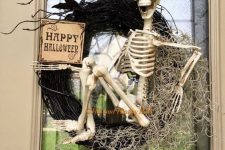 a Halloween wreath of black branches, hay, blackbirds, a sign and a skeleton is a very eye-catchy and creative idea