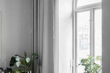 a Scandinavian room with an arched window with a white frame, grey curtains and grey furniture, a woven chair and some greenery