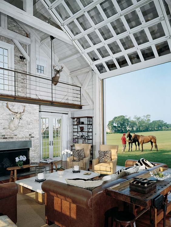 a barn living room with a tall attic ceiling is opened up to the outdoor fields with simple garage doors at once, and indoor becomes outdoor