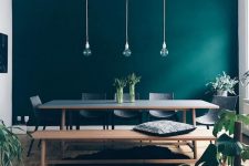 a beautiful Scandi dining room with an emerald accent wall, a dining table, bench and chairs plus pendant bulbs and potted plants