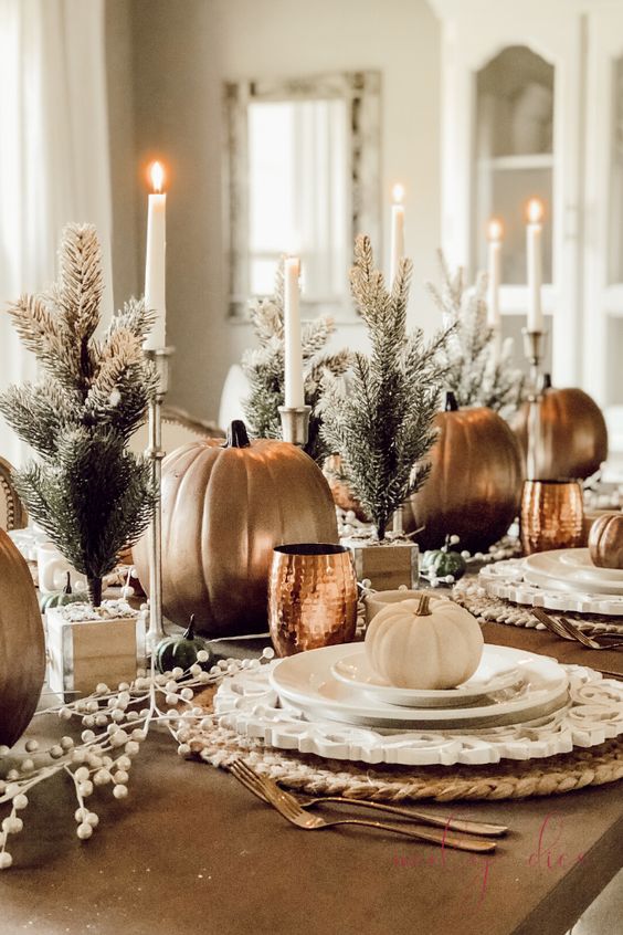 a beautiful Thanksgiving table setting with mini trees, pumpkins, candles, faux berries, copper mugs and woven placemats