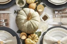 a beautiful rustic Thanksgiving tablescape with pumpkins, candles, greenery, black chargers and neutral napkins and a runner