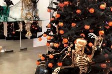 a bold and chic Halloween styled space with a Halloween tree with pumpkin lights, black pumpkins and a gilded skeleton is a fun idea