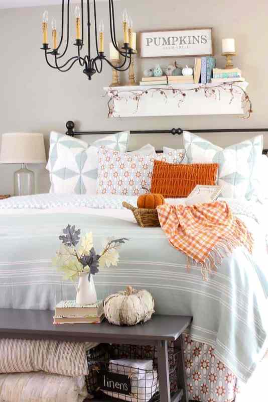 a bold farmhouse bedroom with greige walls, a forged bed with blue and orange printed bedding, a forged chandelier and a grey bench with pumpkins and leaves