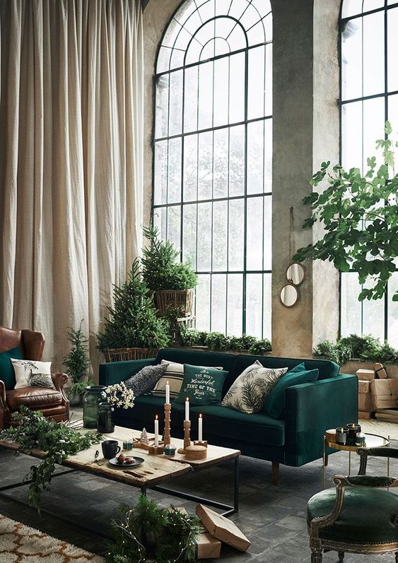 a bold industiral living room styled for Christmas, with double-height arched window, emerald and brown furniture and lots of greenery