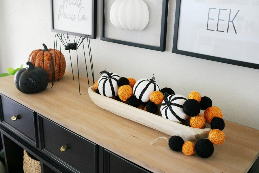 a bowl with black and white pumpkins and orange and black yarn balls, faux pumpkins and a spider candle holder