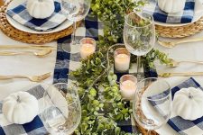 a bright Thanksgiving table setting with a navy plaid runner and napkins, white pumpkins, greenery, candles and woven placemats