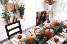 a bright Thanksgiving tablescape with a greenery and pumpkin runner, striped napkins and neutral placemats, a copper kettle
