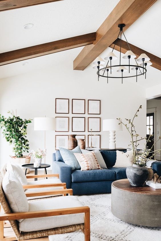 a bright and fresh liivng room with wodoen beams, a blue sofa, neutral chairs, a round coffee table and a grid gallery wall
