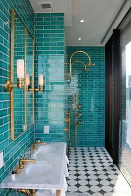 a bright bathroom with turquoise skinny tiles, a pretty black and white floor, a double sink and brass fixtures plus a mirror in a brass frame