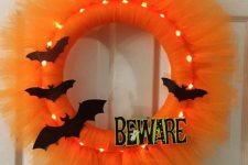 a bright lit up orange tulle Halloween wreath with black bats and letters can be DIYed easily and looks very pretty