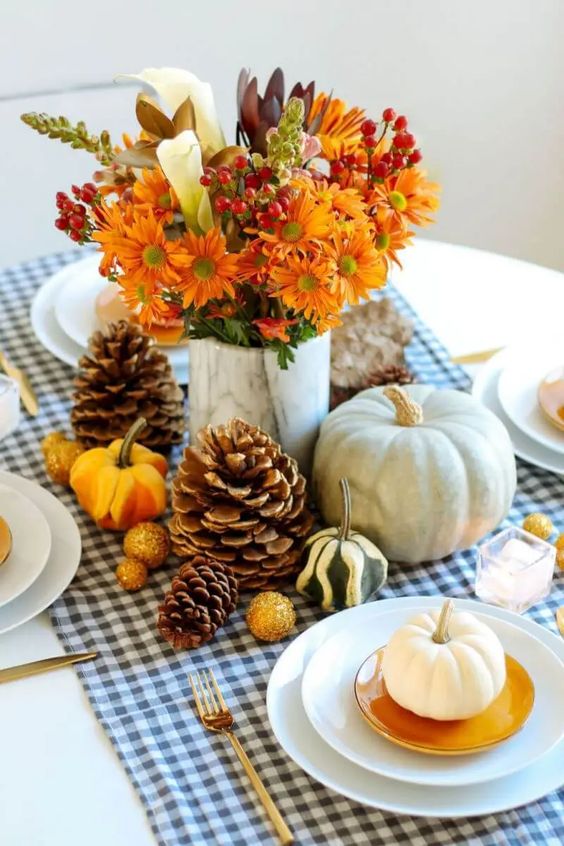 a bright rustic Thanksgiving tablescape with a plaid runner, gourds and pinecones, bold blooms, berries and neutral pumpkins is fresh
