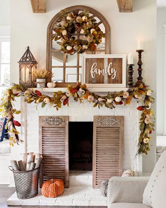 a bright rustic fall mantel with a reclaimed sign, bright leaves and pumpkins, candle lanterns, wooden candleholders with pillar candles and shutters