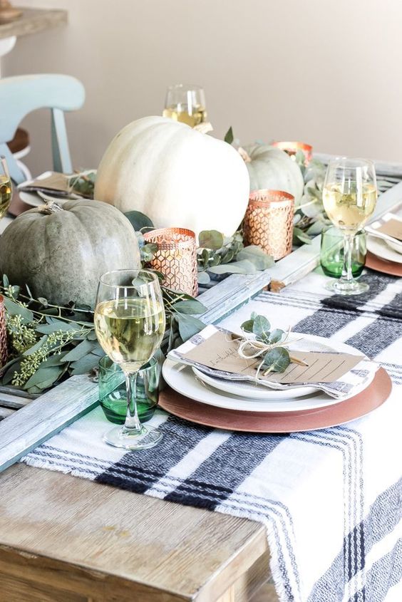 a casual rustic Thanksgiving table with a striped tablecloth, heirloom pumpkins and eucalyptus, green glasses and copper chargers