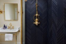 a catchy bathroom with neutral walls, a shower space clad with black and grey chevron tiles, brass and gold fixtures is super chic and shiny