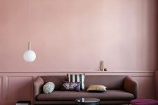 a catchy living room with a pink paneled accent wall, a dusty pink sofa, a purple pouf, a color block rug and a burgundy ceiling