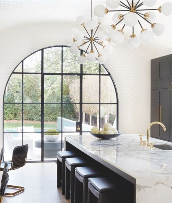 a chic black and white kitchen with an oversized arched window that includes the door to the garden and is a fantastic solution to add more chic