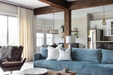 a chic living room with dark wooden beams and a pillar, a blue sofa, a brown leather chair and a duo of industrial coffee tables