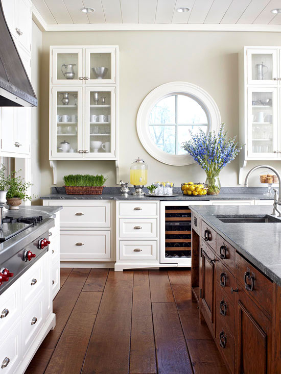 a chic rustic kitchen with white and stained furniture, a porthole window and lots of greenery and blooms