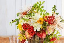 a colorful Thanksgiving tablescape with a wood slice, corn cobs with bright blooms and berries, a striped tablecloth and green napkins