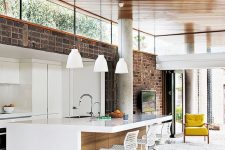 a contemporary space with a brick wall, white sleek cabinetry, pendant lamps and clerestory windows that birng light in