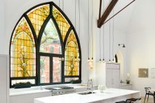 a contemporary to minimalist kitchen done in white, with wooden beams and bulbs hanging and a unique Gothic-style window with stained glass