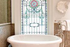 a cool bathroom with tan tiles and white walls, an oval tub on clawfoot legs and a stained glass window is a stylish space