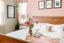 a cozy bedroom with a peachy pink wall, a stained bed, neutral and pink bedding, a grid gallery wall, a beaded chandelier and some potted plants