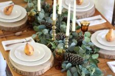 a cozy rustic woodland Thanksgiving tablescape with a greenery and pinecone runner, candles, wood slices and gilded pears