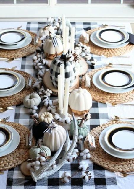 a cute farmhouse Thanksgiving tablescape with a buffalo tablecloth and a pumpkin, white and black pumpkins, cotton, antlers and woven placemats