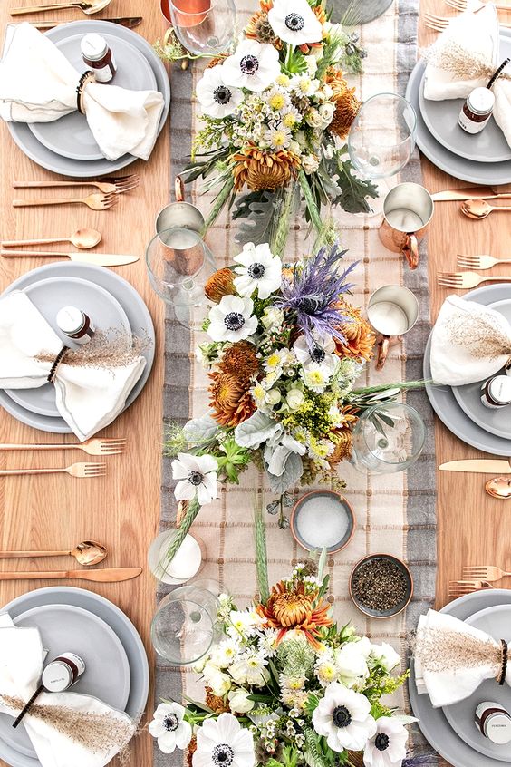 a delicate and cool Thanksgiving tablescape with a plaid runner, grey plates, white and purple blooms, candles