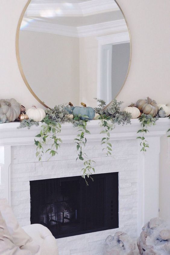 a delicate and subtle mantel decor with pastel and white pumpkins, gilded faux ones and cascading greenery plus an oversized round mirror