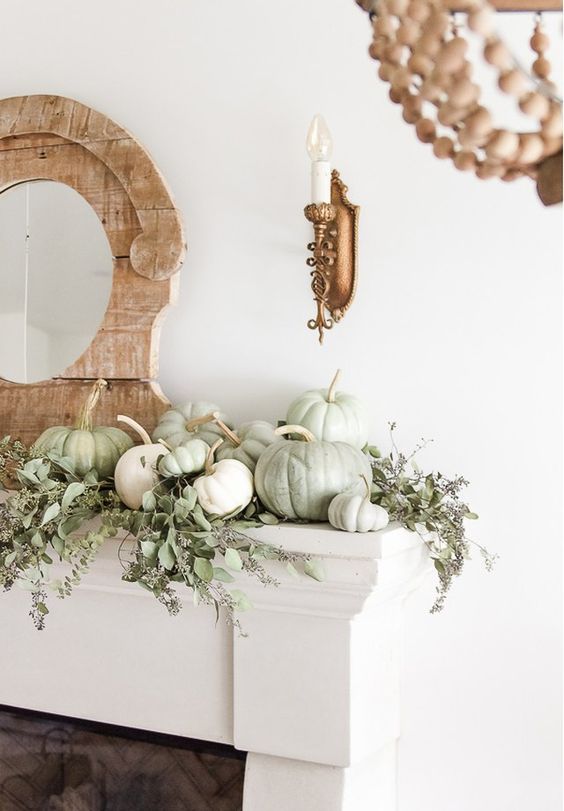 a delicate farmhouse fall mantel with lots of greenery and white and light green natural pumpkins plus a mirror in a wooden frame